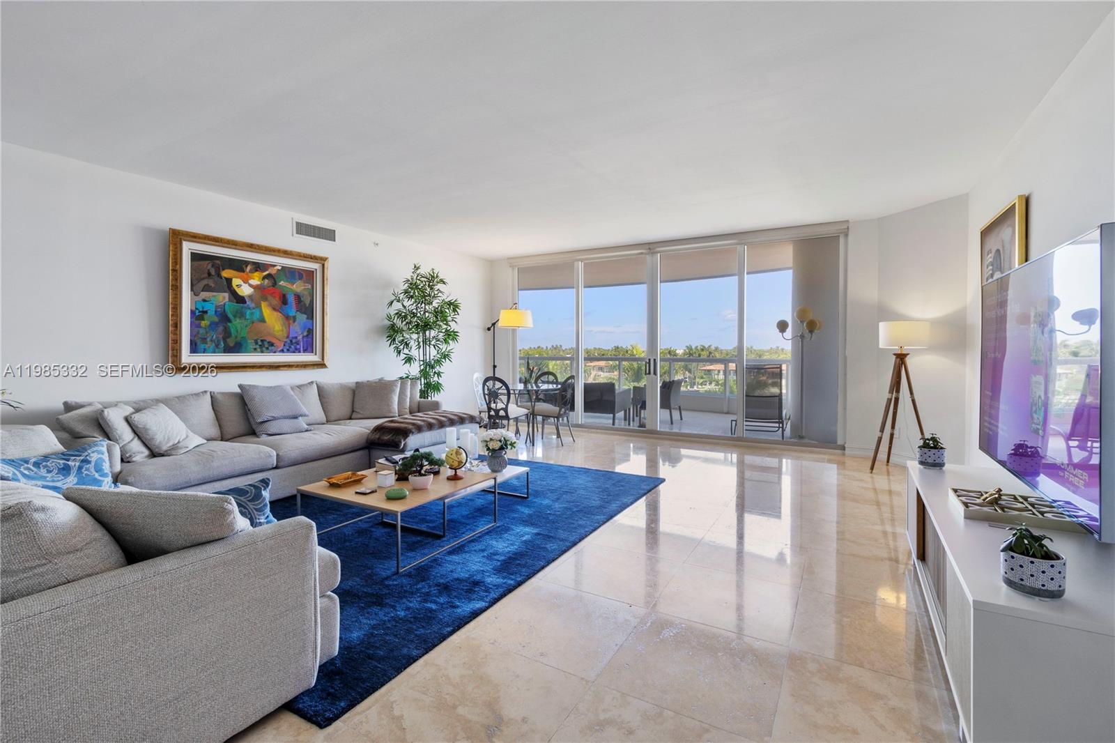 A bright living room features a large blue area rug, gray sectional sofa, and balcony access — 21050 Point Pl # 604, Aventura FL 33180, AVENTURA, FL