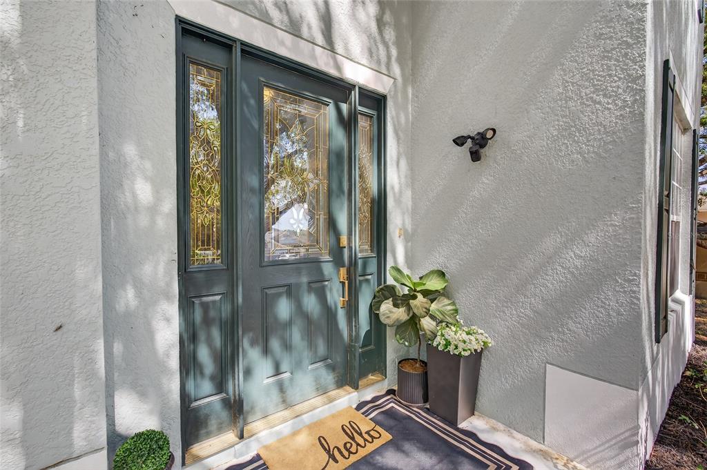A dark green front door with glass panels sits beside a potted plant and mat — 1305 WINDY BLUFF DRIVE, MINNEOLA, FL