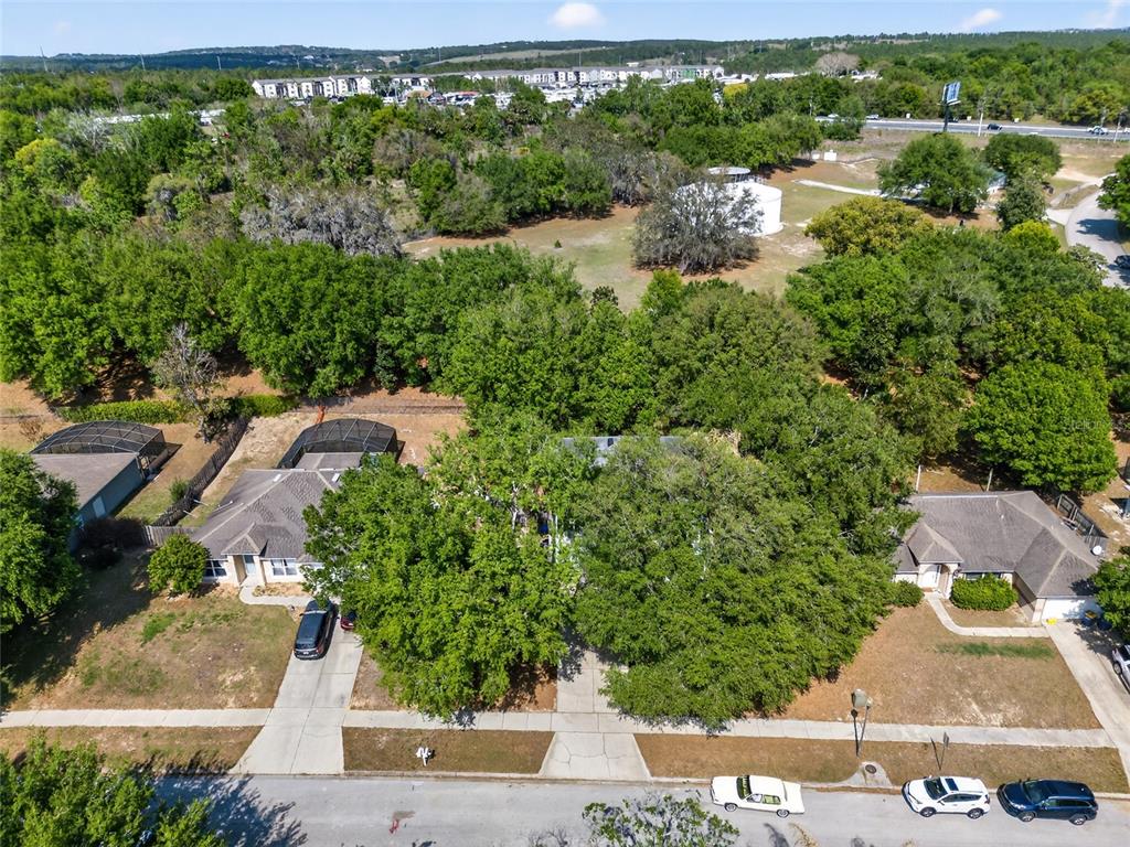 An aerial view shows three suburban houses with driveways and large trees in a neighborhood — 1305 WINDY BLUFF DRIVE, MINNEOLA, FL