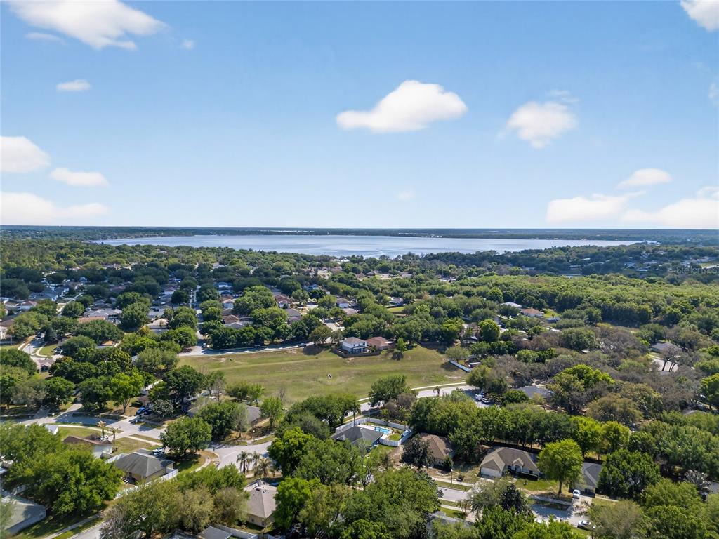 An aerial view shows a residential neighborhood with a large grassy field and a lake — 1305 WINDY BLUFF DRIVE, MINNEOLA, FL