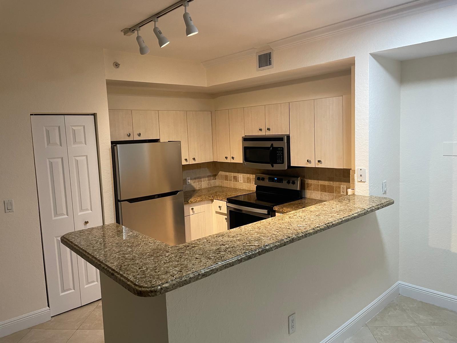 A kitchen features light wood cabinets, stainless steel appliances, and a granite-topped breakfast bar — 1803 N Flagler Drive # 212, West Palm Beach FL 33407, WEST PALM BEACH, FL