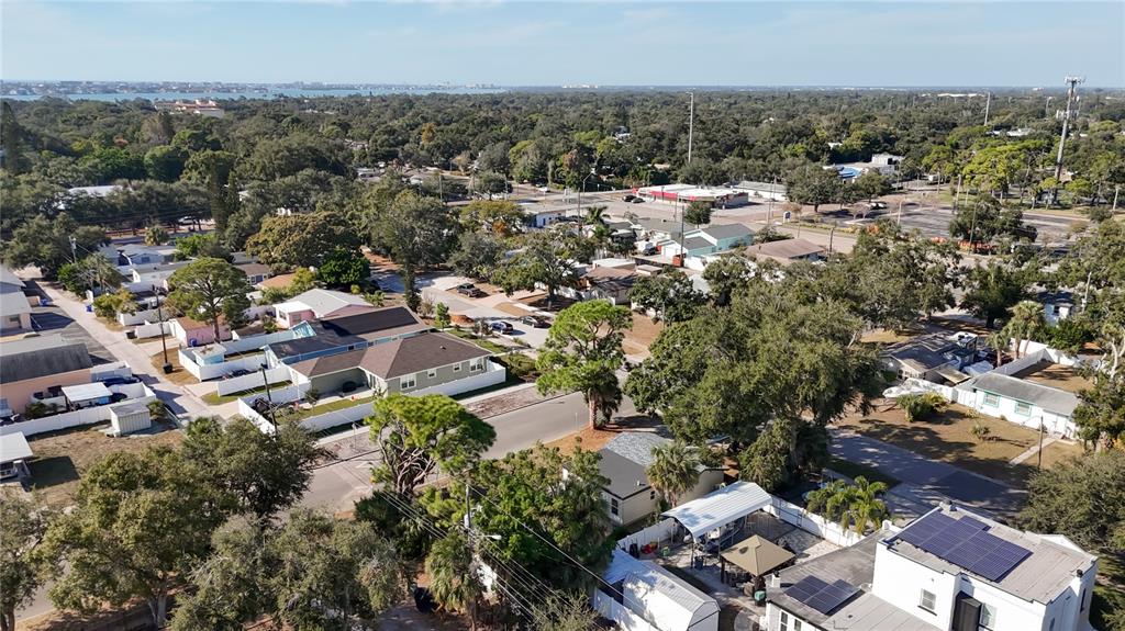 An aerial view shows a residential neighborhood with houses, trees, and a distant body of water — 6948 DARTMOUTH AVENUE N, ST PETERSBURG, FL