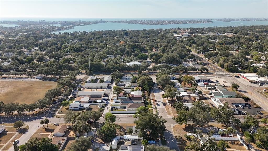 An aerial view shows a residential neighborhood with houses, trees, and a distant body of water — 6948 DARTMOUTH AVENUE N, ST PETERSBURG, FL
