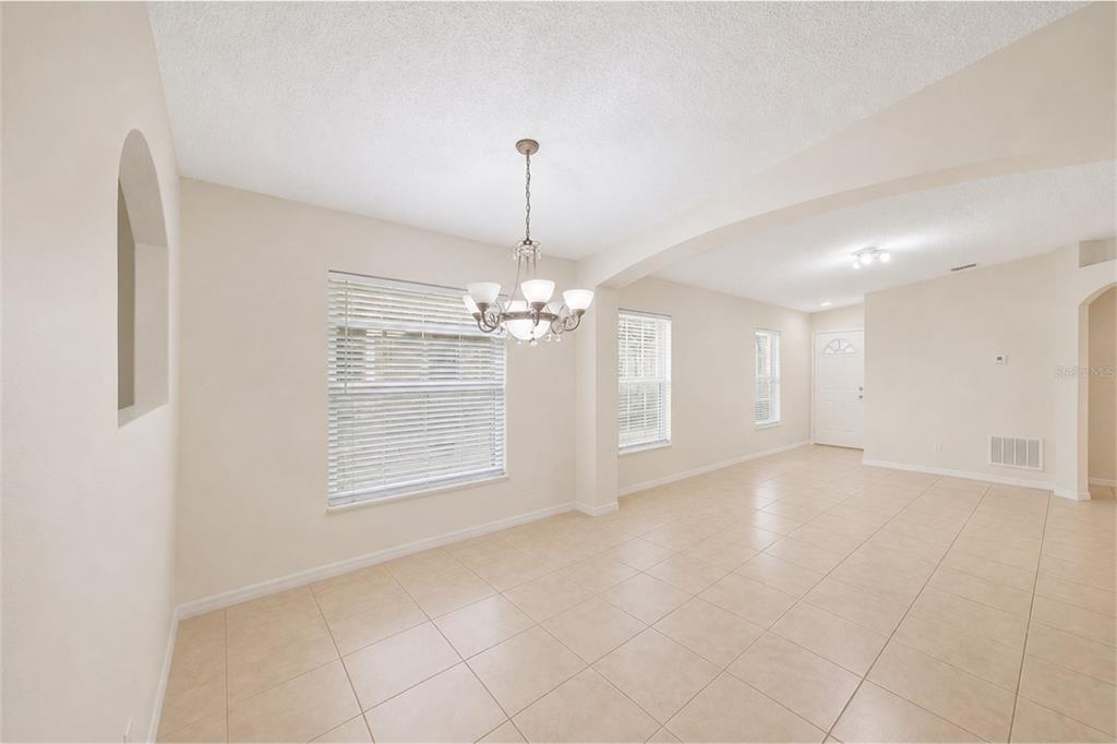 A bright dining area with tile floors, a chandelier, and an arched wall niche — 2848 OSPREY COVE PLACE UNIT 204, KISSIMMEE, FL