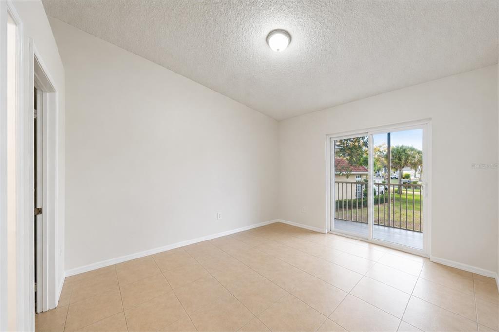 An empty room with beige tile flooring, white walls, and a sliding glass door — 2848 OSPREY COVE PLACE UNIT 204, KISSIMMEE, FL