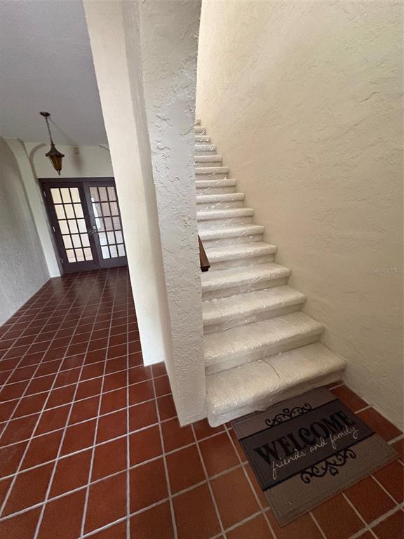 A staircase covered in protective plastic leads upward next to a tiled entryway and door — 15810 REDINGTON DRIVE, REDINGTON BEACH, FL