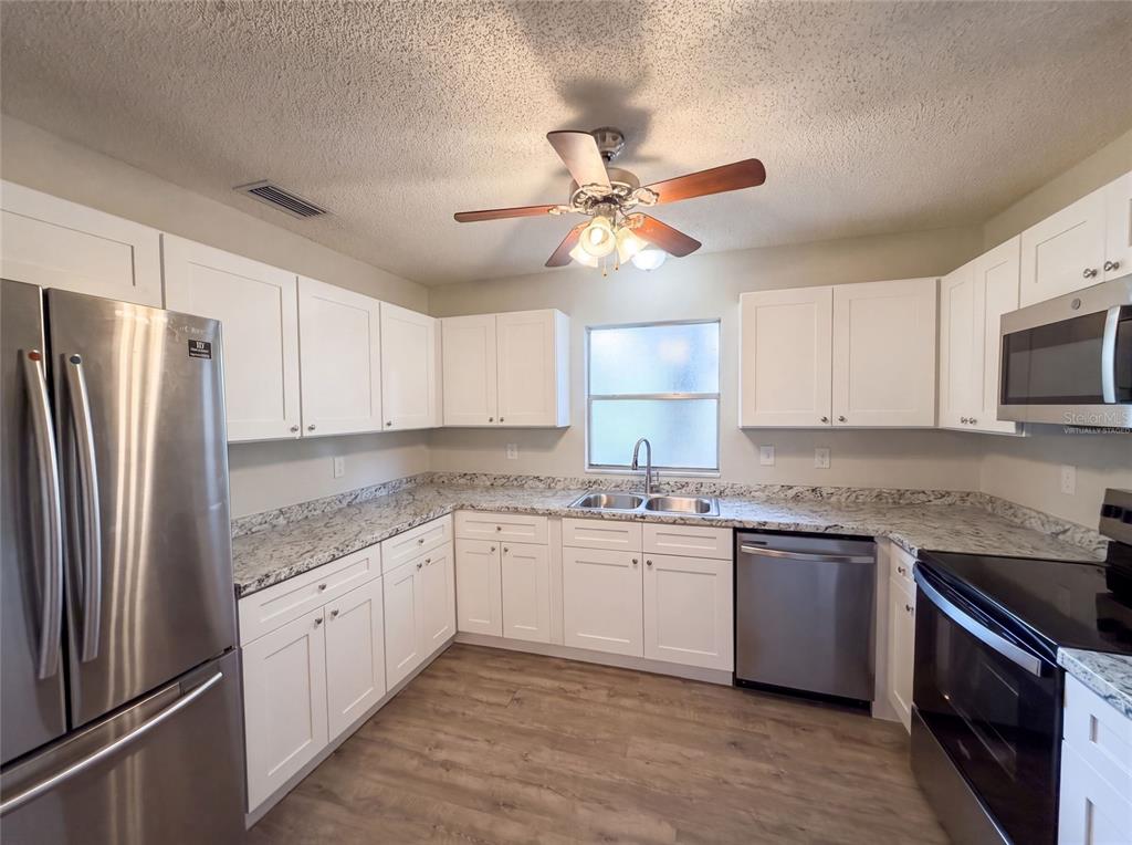 A kitchen with white cabinets, stainless steel appliances, granite countertops, and wood-look flooring — 5750 NW 55TH AVENUE, OCALA, FL