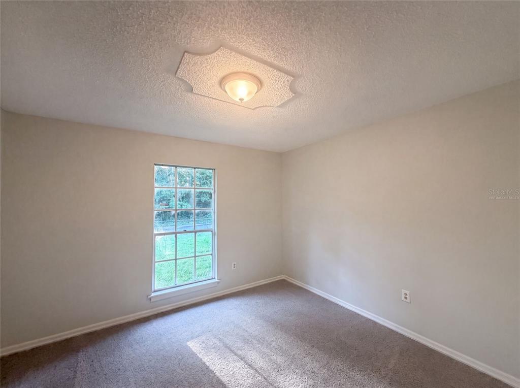 An empty bedroom features beige walls, carpeted flooring, a single window, and a ceiling light — 5750 NW 55TH AVENUE, OCALA, FL