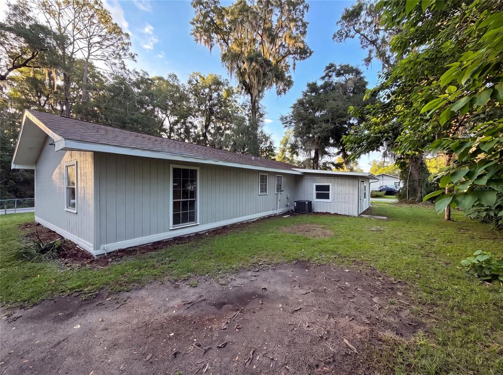 The exterior of a light-gray, single-story house features a shingled roof and surrounding trees — 5750 NW 55TH AVENUE, OCALA, FL