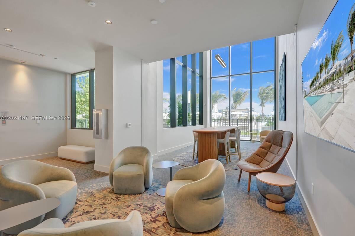 A modern lounge area features floor-to-ceiling windows, plush armchairs, and a high-top table — 580 72 ST # 1804, Miami Beach 34553, MIAMI BEACH, FL