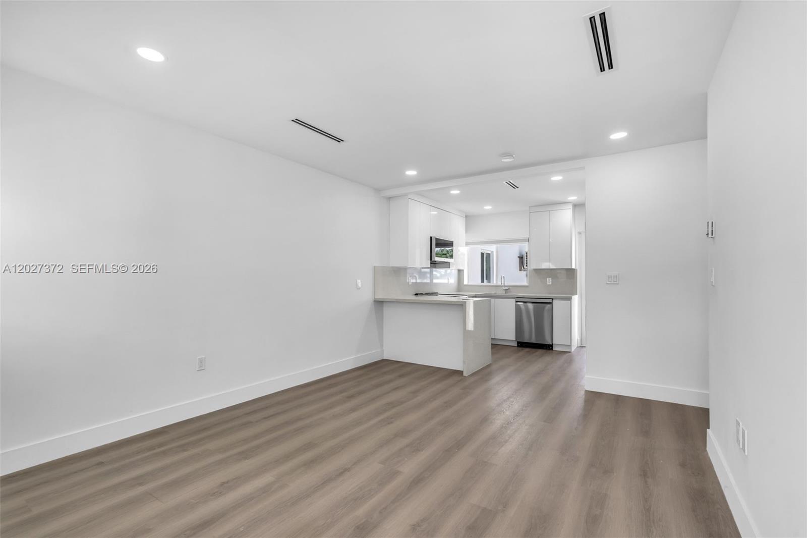 A minimalist kitchen with white cabinetry and stainless steel appliances opens to a living area — 2814 SW 26th St # 2814, Miami FL 33133, MIAMI, FL