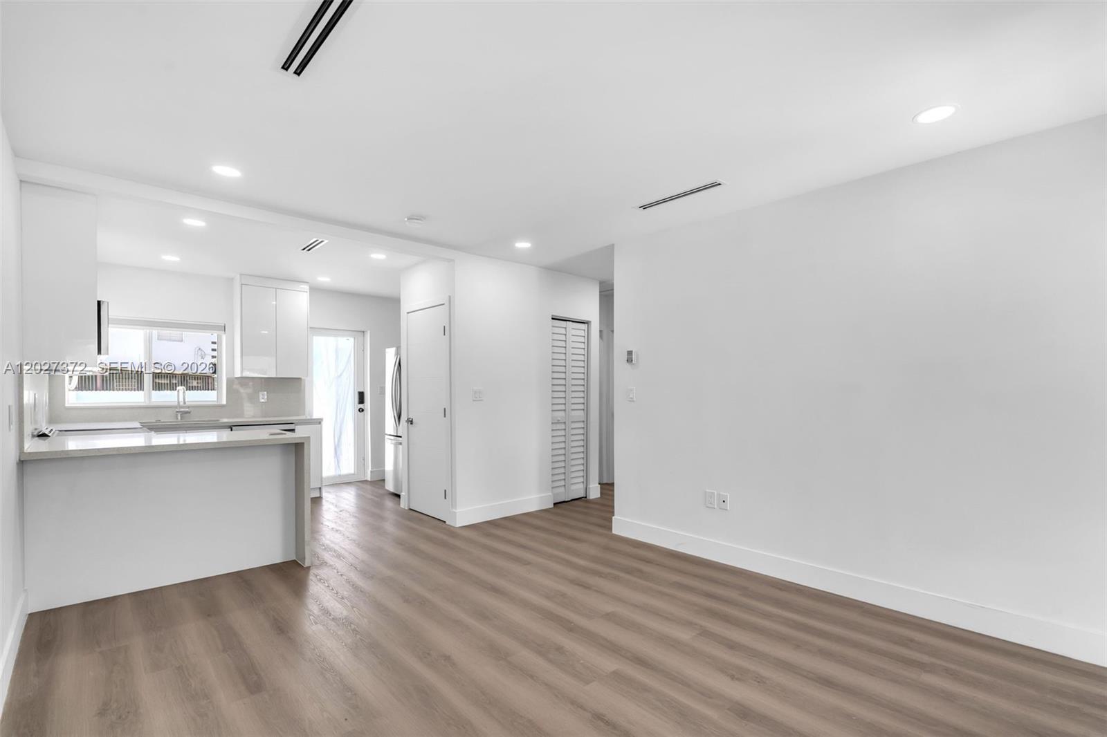 A bright, open-concept kitchen and living area features white cabinetry and light wood-look flooring — 2814 SW 26th St # 2814, Miami FL 33133, MIAMI, FL