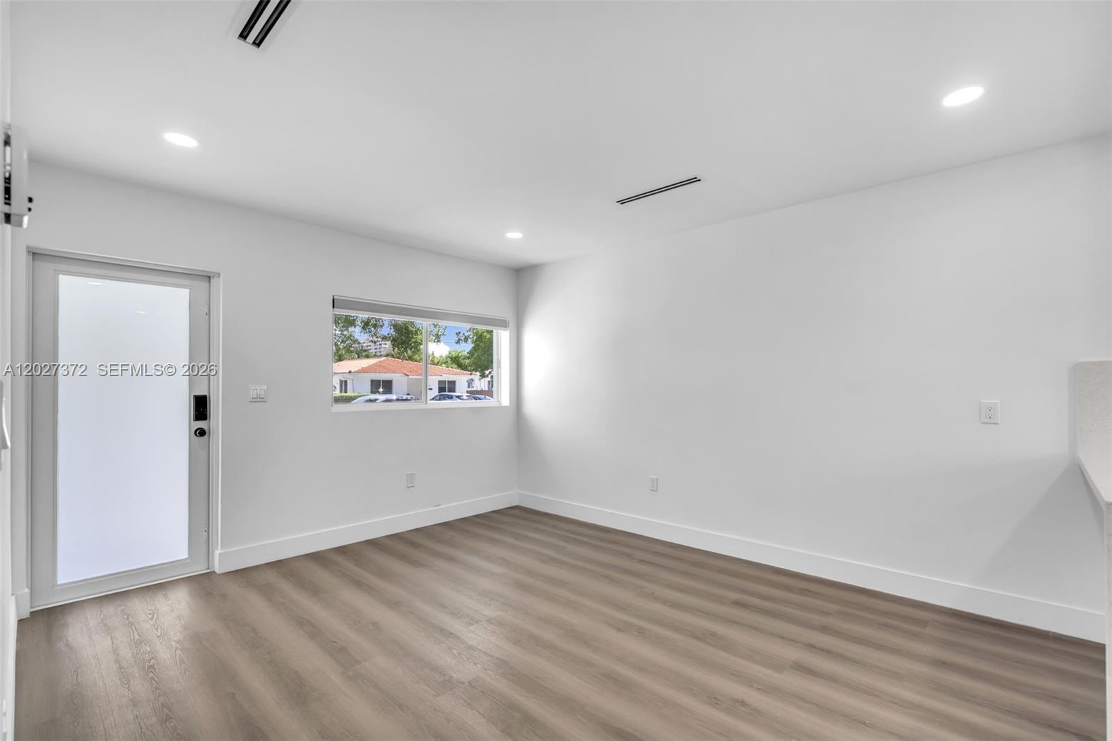An empty room features white walls, light wood-look flooring, a glass-paneled door, and a window — 2814 SW 26th St # 2814, Miami FL 33133, MIAMI, FL