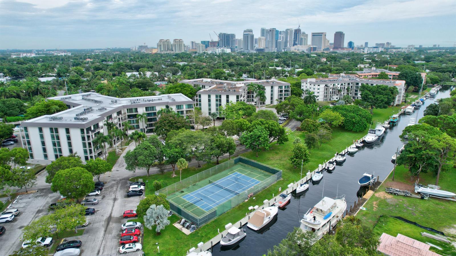 An aerial view shows apartment buildings, a tennis court, and boats docked in a canal — 1101 River Reach Drive # 415, Fort Lauderdale FL 33315, FORT LAUDERDALE, FL