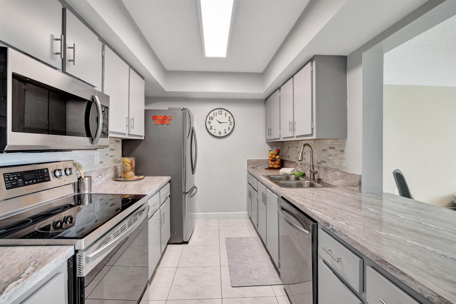 A galley kitchen features gray cabinets, stainless steel appliances, and light-colored stone countertops — 1101 River Reach Drive # 415, Fort Lauderdale FL 33315, FORT LAUDERDALE, FL