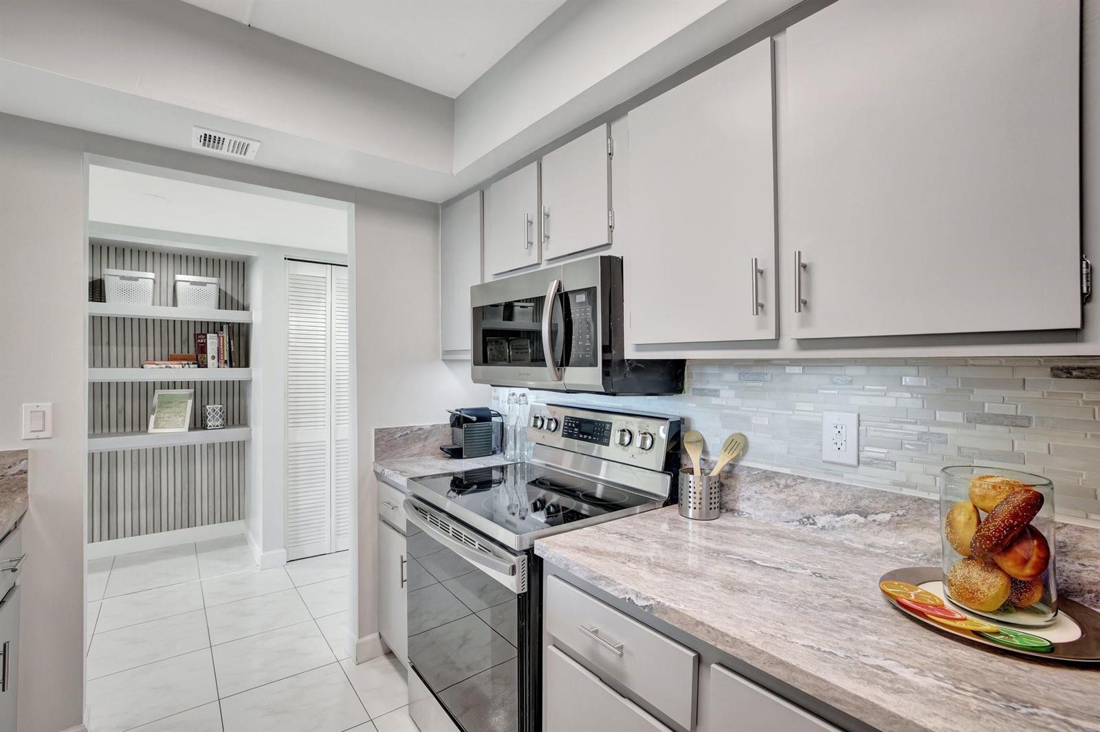 A kitchen features gray cabinets, stainless steel appliances, a stone countertop, and an adjacent pantry — 1101 River Reach Drive # 415, Fort Lauderdale FL 33315, FORT LAUDERDALE, FL