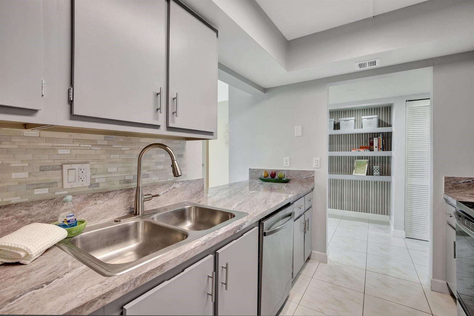 A kitchen features gray cabinets, stone-look countertops, a double sink, and an adjacent pantry area — 1101 River Reach Drive # 415, Fort Lauderdale FL 33315, FORT LAUDERDALE, FL
