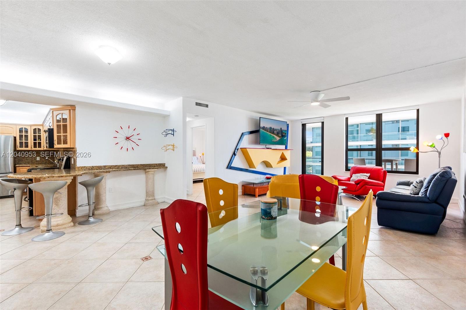 An open-concept living and dining area features colorful furniture, a glass table, and kitchen bar — 10185 Collins Ave # 521, Bal Harbour FL 33154, BAL HARBOUR, FL