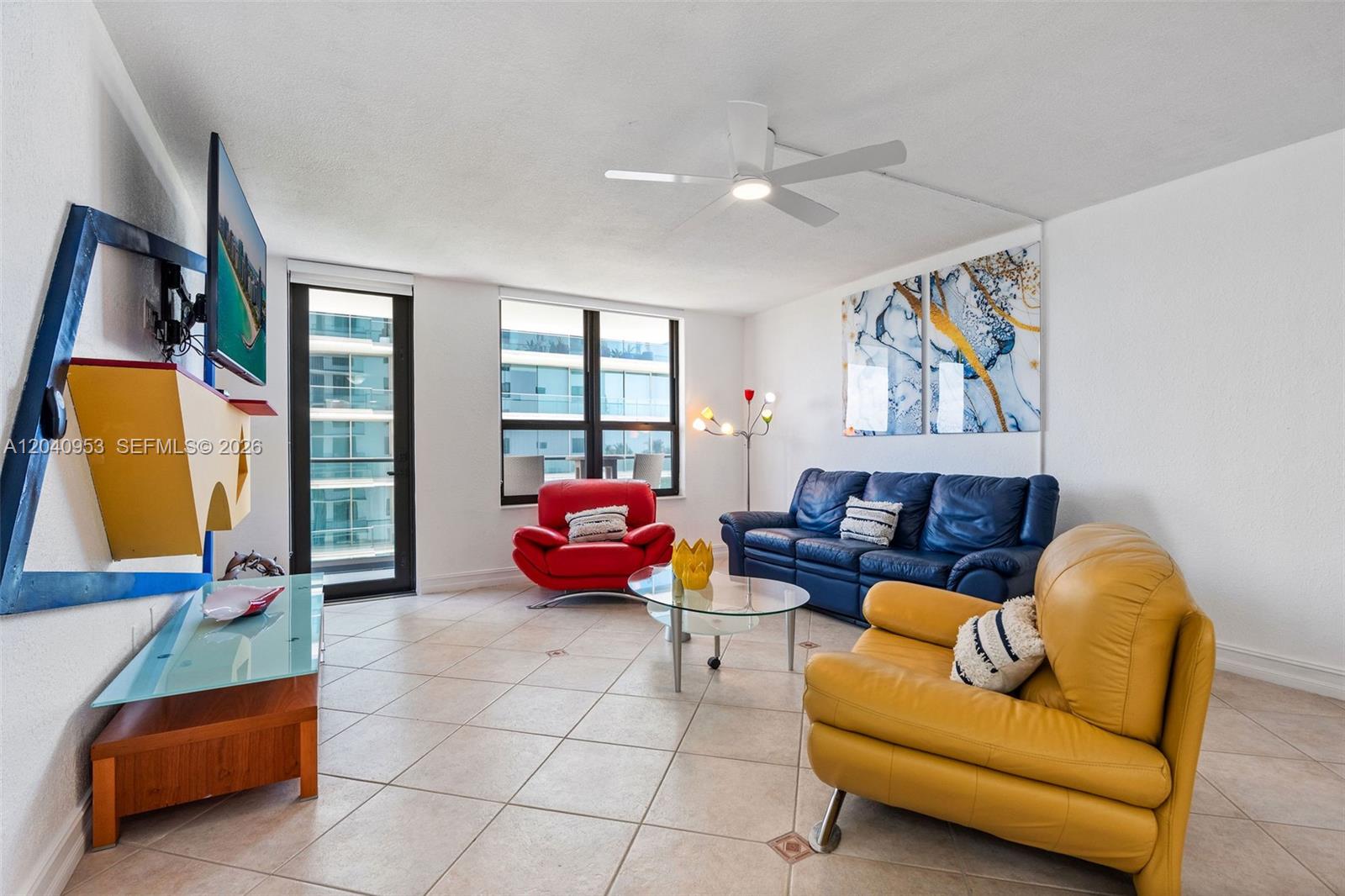 A living room features tile floors, a ceiling fan, and colorful leather furniture — 10185 Collins Ave # 521, Bal Harbour FL 33154, BAL HARBOUR, FL