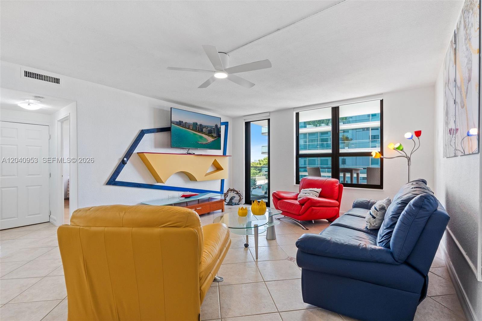 A living room features a blue sofa, red armchair, yellow chair, and a wall-mounted television — 10185 Collins Ave # 521, Bal Harbour FL 33154, BAL HARBOUR, FL