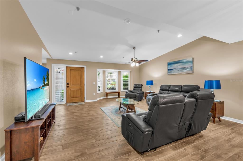 A living room features wood-look tile flooring, a leather sofa set, and a large television — 2350 HARBOUR OAKS DRIVE, LONGBOAT KEY, FL