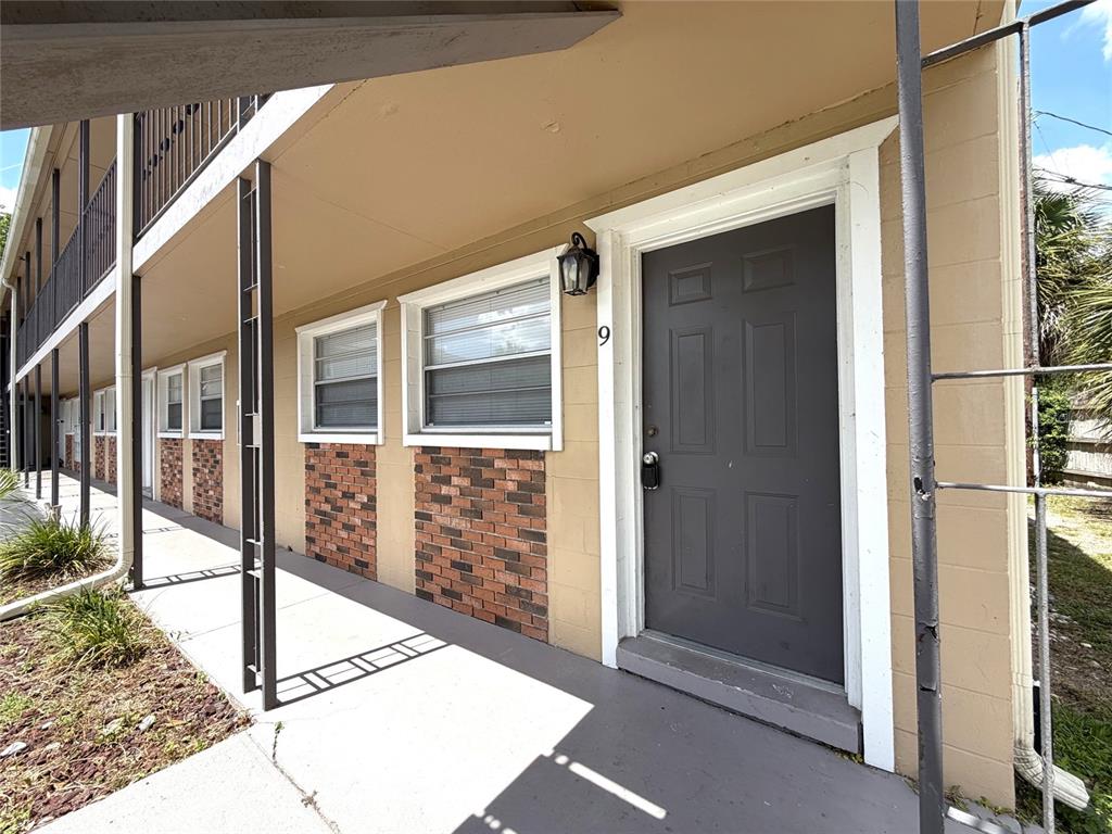 The exterior of a ground-floor apartment unit features a dark door, brick accents, and windows — 501 NW 15TH AVENUE UNIT 9, GAINESVILLE, FL
