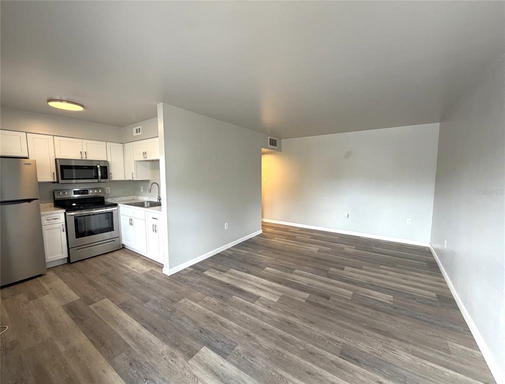 An open-concept living room and kitchen featuring wood-look flooring, white cabinetry, and a patterned rug — 501 NW 15TH AVENUE UNIT 9, GAINESVILLE, FL