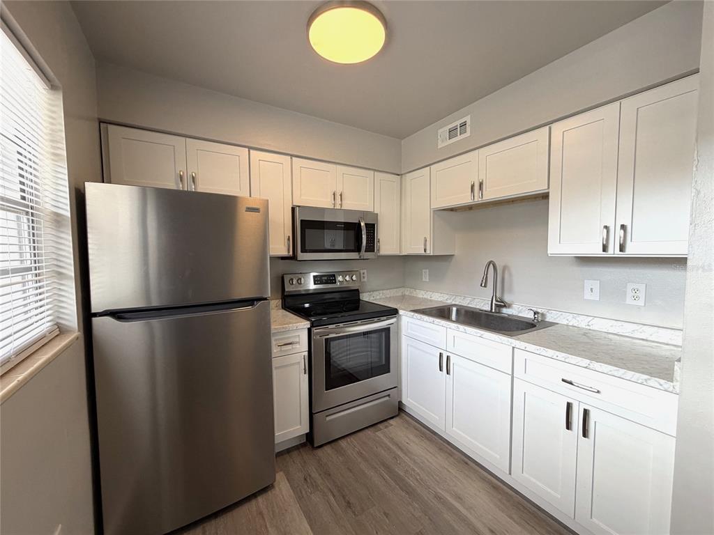 A kitchen with stainless steel appliances and white cabinets opens into a living area — 501 NW 15TH AVENUE UNIT 9, GAINESVILLE, FL