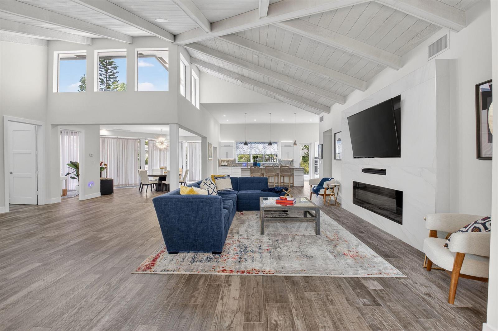 A spacious living room features a blue sectional, vaulted ceilings, and a modern fireplace wall — 4869 Pineview Circle, Delray Beach FL 33445, DELRAY BEACH, FL