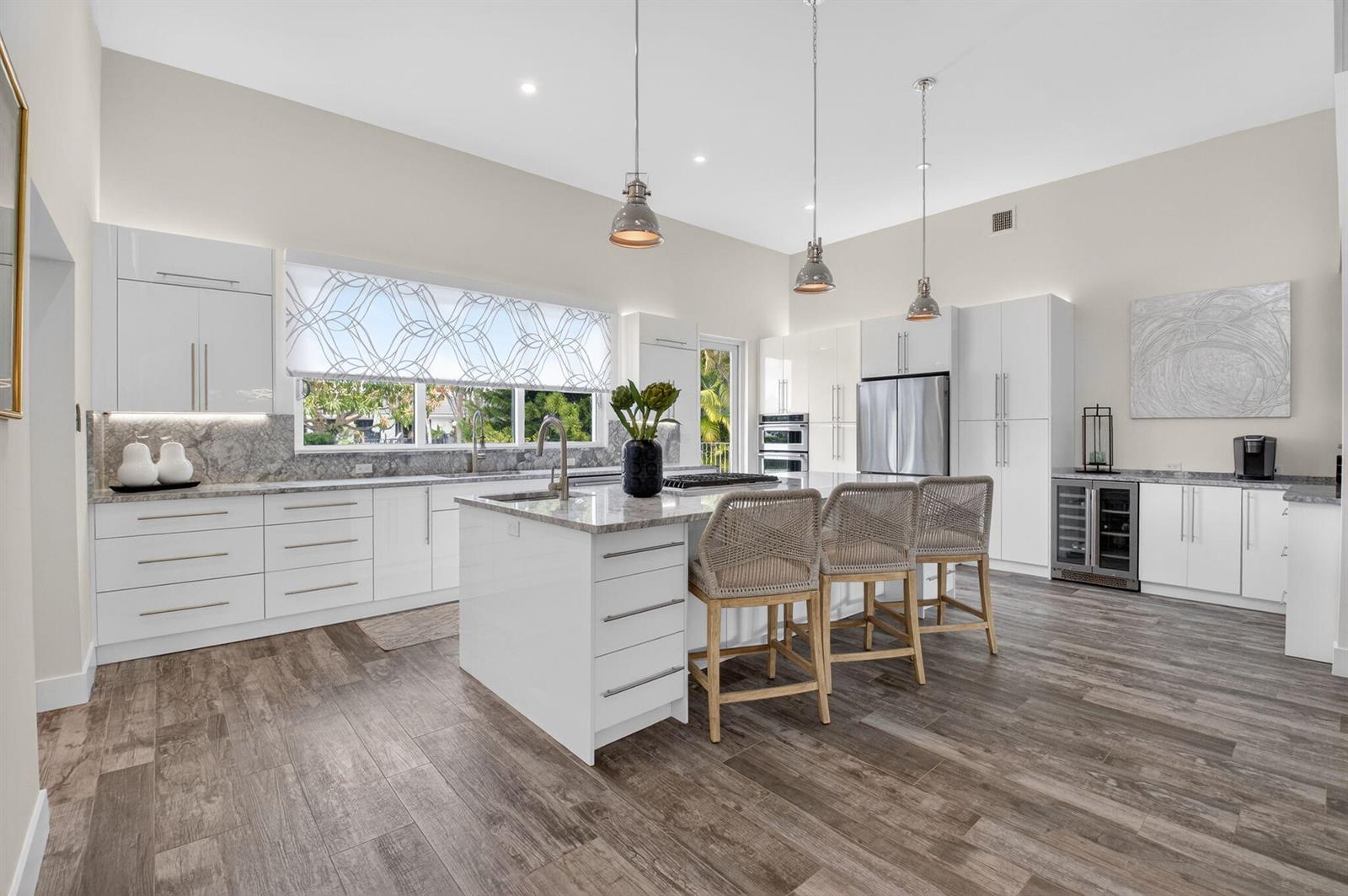 A modern white kitchen features a central island, stainless steel appliances, and wood-look tile flooring — 4869 Pineview Circle, Delray Beach FL 33445, DELRAY BEACH, FL