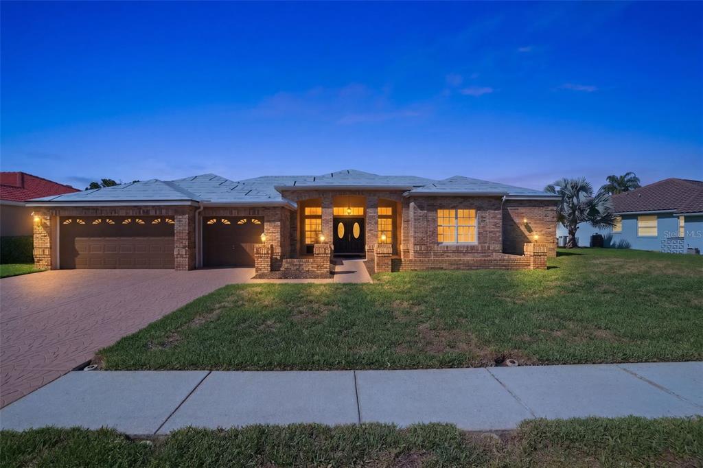 A single-story brick house with a two-car garage and a paved driveway at dusk — 3166 STERLING STREET, TARPON SPRINGS, FL