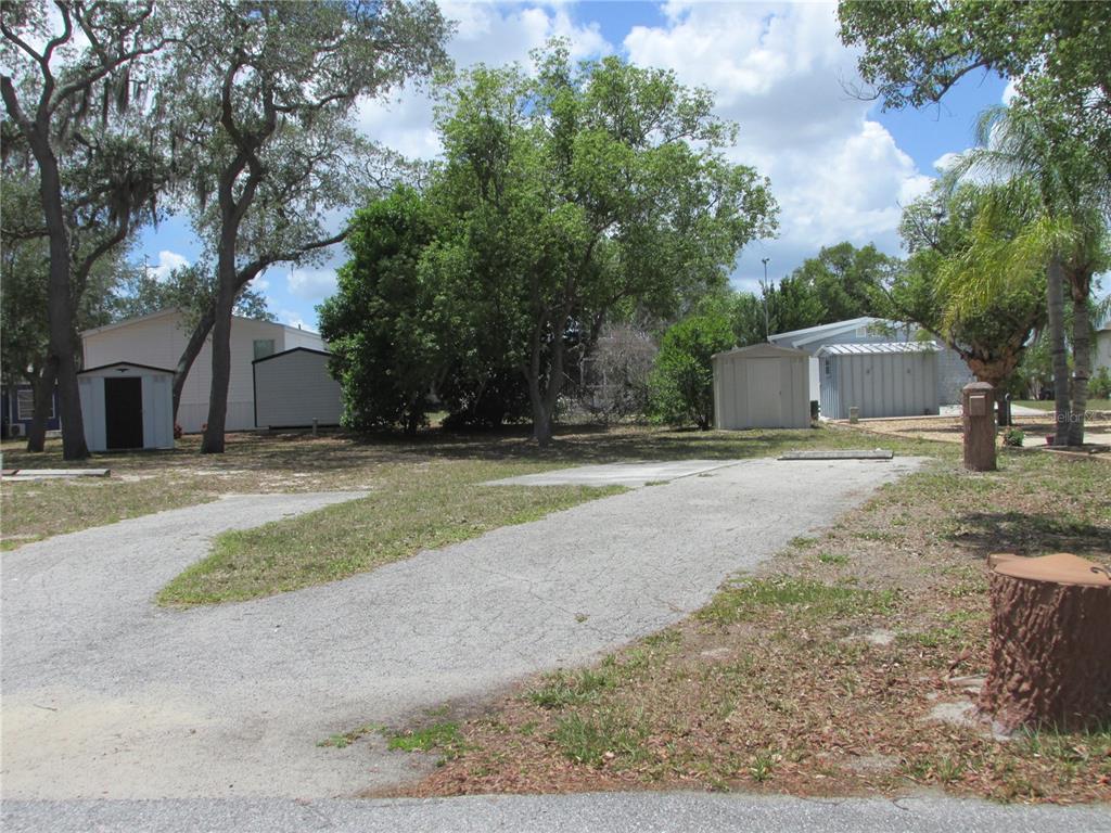 A gravel driveway leads to a grassy lot with several storage sheds and mature trees — 20 SILVER DOCTOR LANE, LAKE WALES, FL