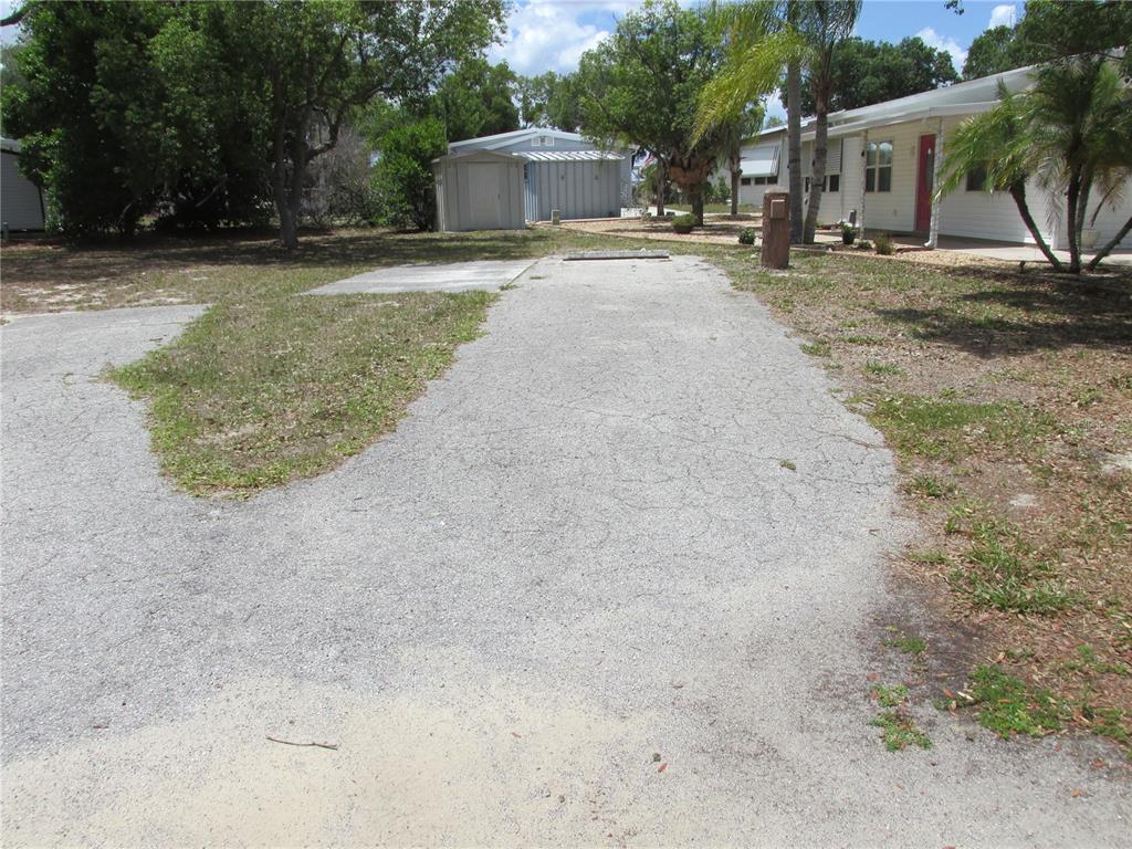 A gravel driveway leads toward a small storage shed and a white mobile home — 20 SILVER DOCTOR LANE, LAKE WALES, FL