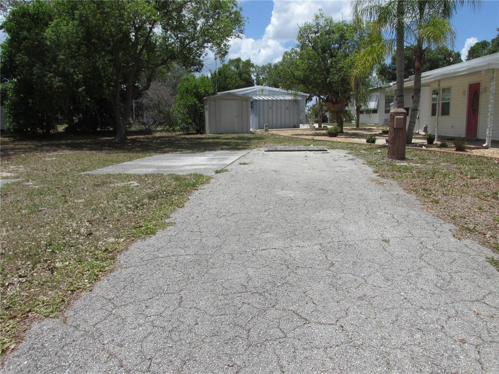 A cracked asphalt driveway leads toward a small shed and a house with a red door — 20 SILVER DOCTOR LANE, LAKE WALES, FL