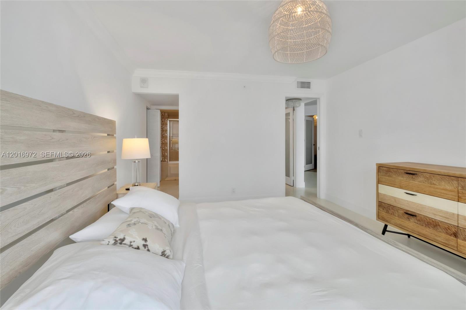A bedroom features a light wood headboard, a white bed, and a wooden dresser — 2401 Collins Ave # 1805, Miami Beach FL 33140, MIAMI BEACH, FL
