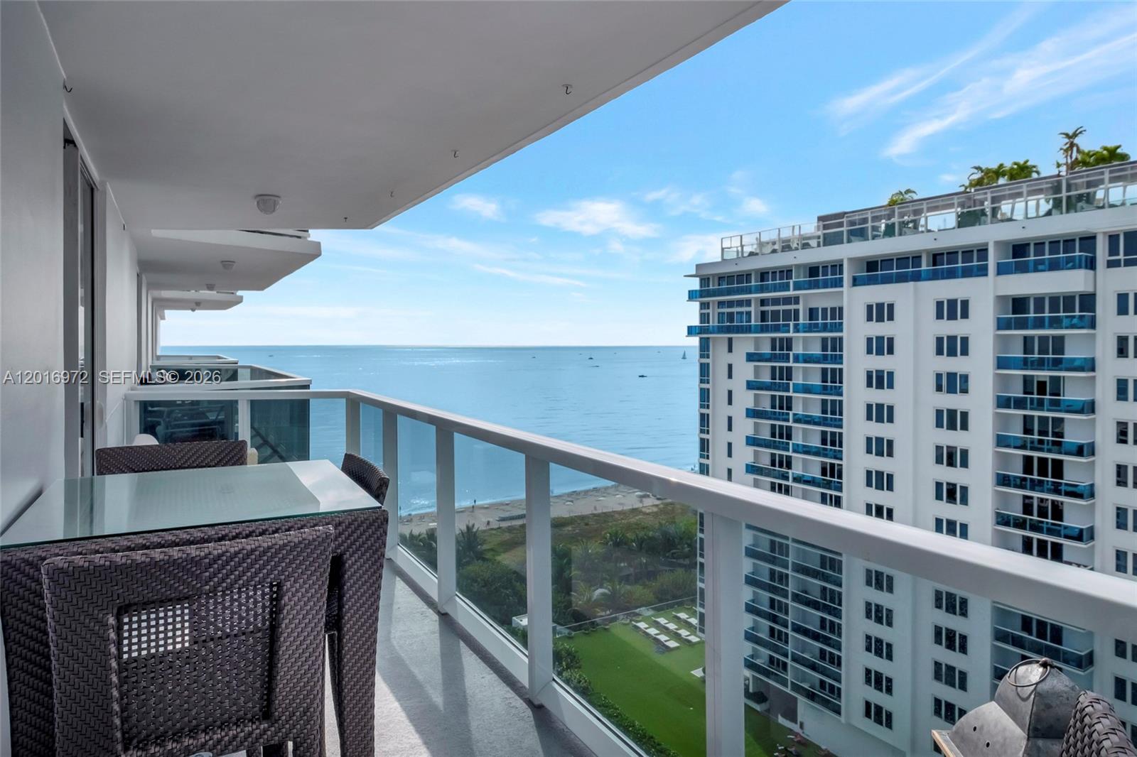 A balcony with outdoor furniture overlooks the ocean and a neighboring high-rise building — 2401 Collins Ave # 1805, Miami Beach FL 33140, MIAMI BEACH, FL