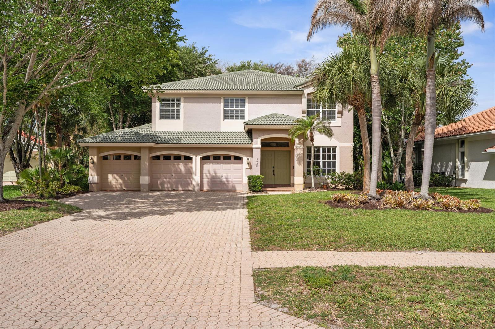 A two-story house with a three-car garage, green tile roof, and a paved driveway — 5020 SW Elk River Court, Palm City FL 34990, PALM CITY, FL