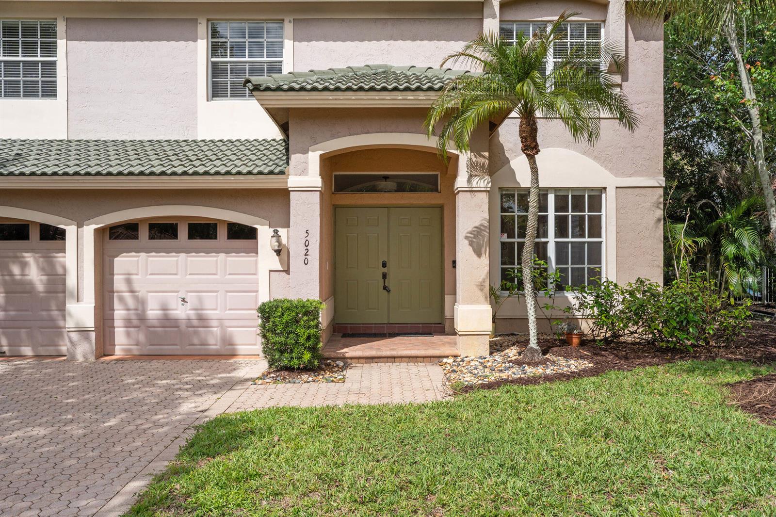 A two-story house exterior features a paved driveway, a double-door entrance, and a palm tree — 5020 SW Elk River Court, Palm City FL 34990, PALM CITY, FL