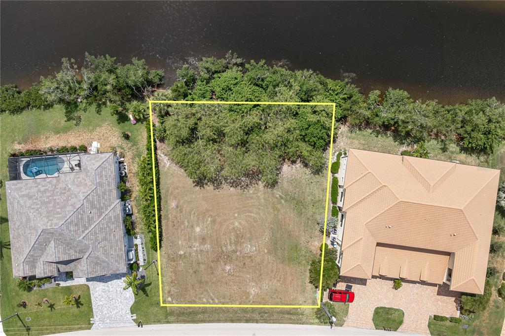 An aerial view shows a vacant rectangular lot situated between two houses along a waterway — 2053 PADRE ISLAND DRIVE, PUNTA GORDA, FL