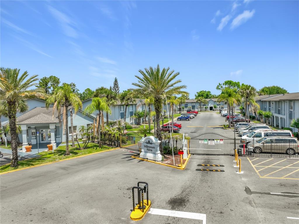 The gated entrance to the Millennium Palms apartment complex features palm trees and parked cars — 4805 S TEXAS AVENUE UNIT 4805A, ORLANDO, FL