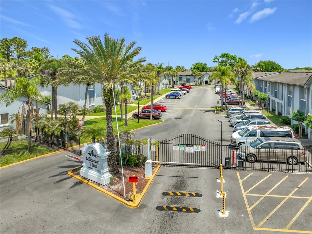 An exterior view of the Millennium Palms gated entrance with parked cars and palm trees — 4805 S TEXAS AVENUE UNIT 4805A, ORLANDO, FL
