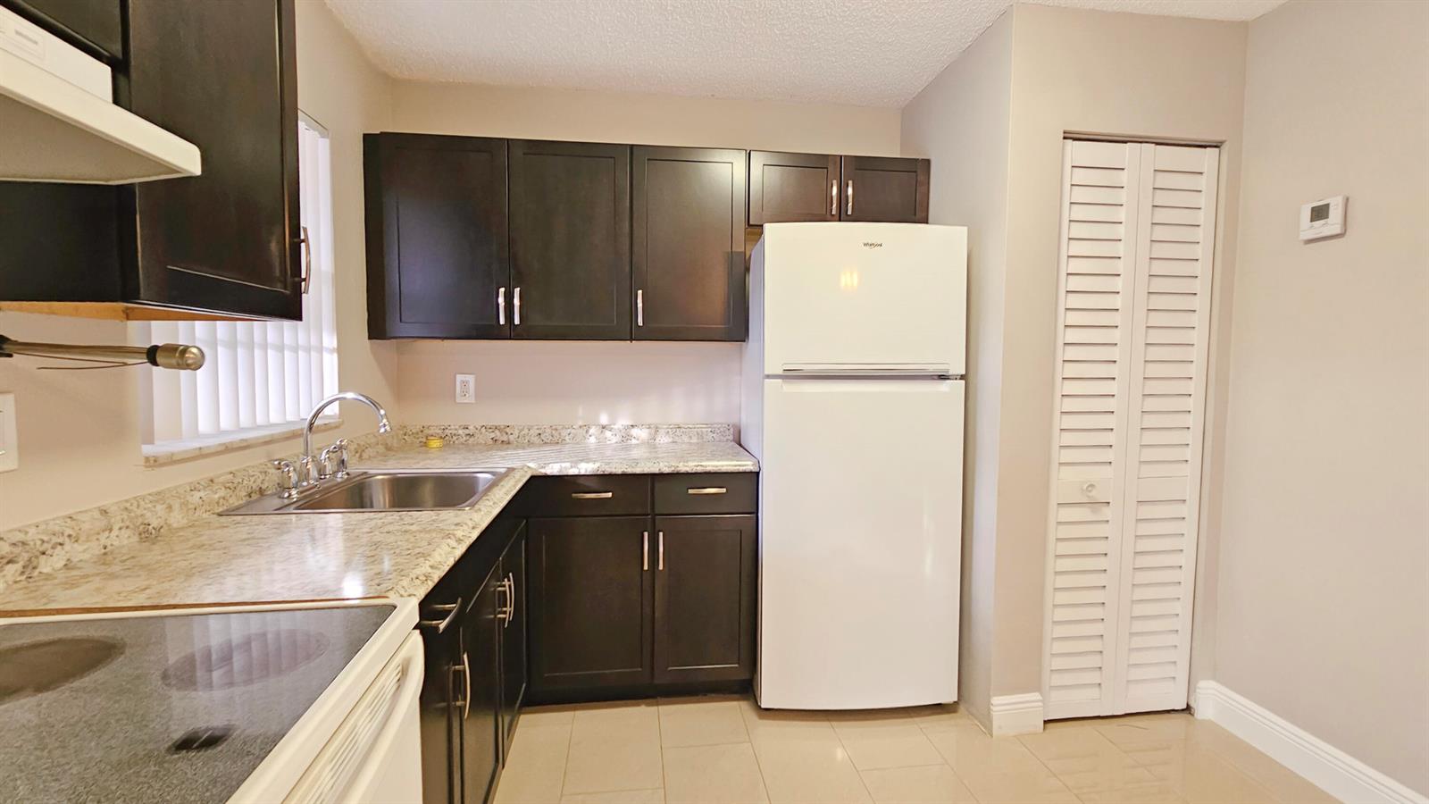 A kitchen features dark wood cabinets, granite countertops, a white refrigerator, and tile flooring — 416 Lakeside Drive # 129, Margate FL 33063, MARGATE, FL