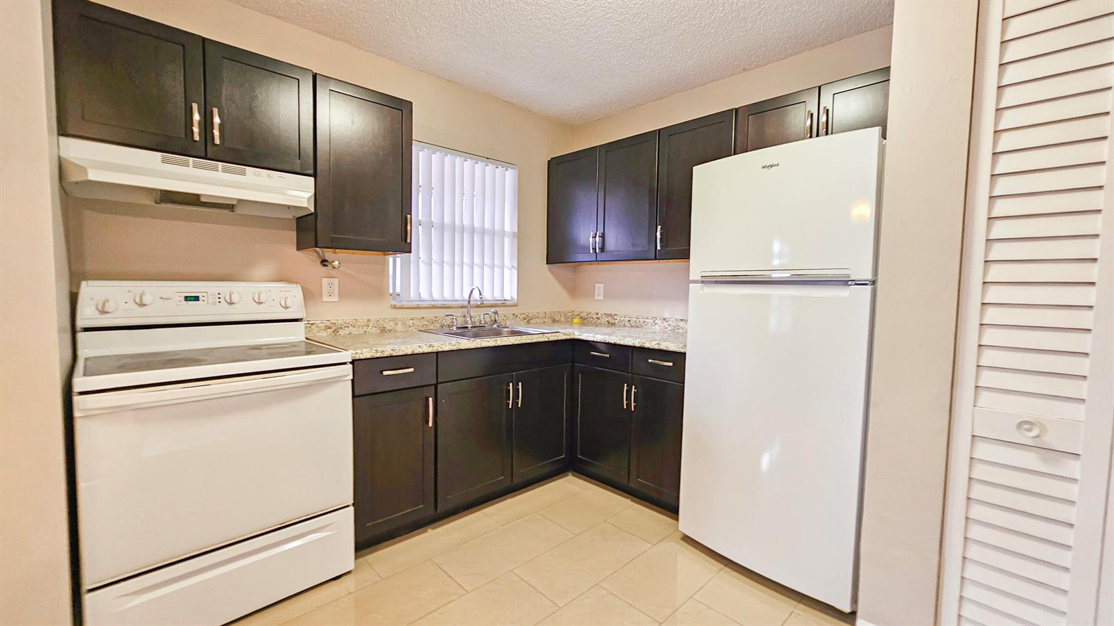 A kitchen features dark wood cabinets, white appliances, and light-colored countertops — 416 Lakeside Drive # 129, Margate FL 33063, MARGATE, FL