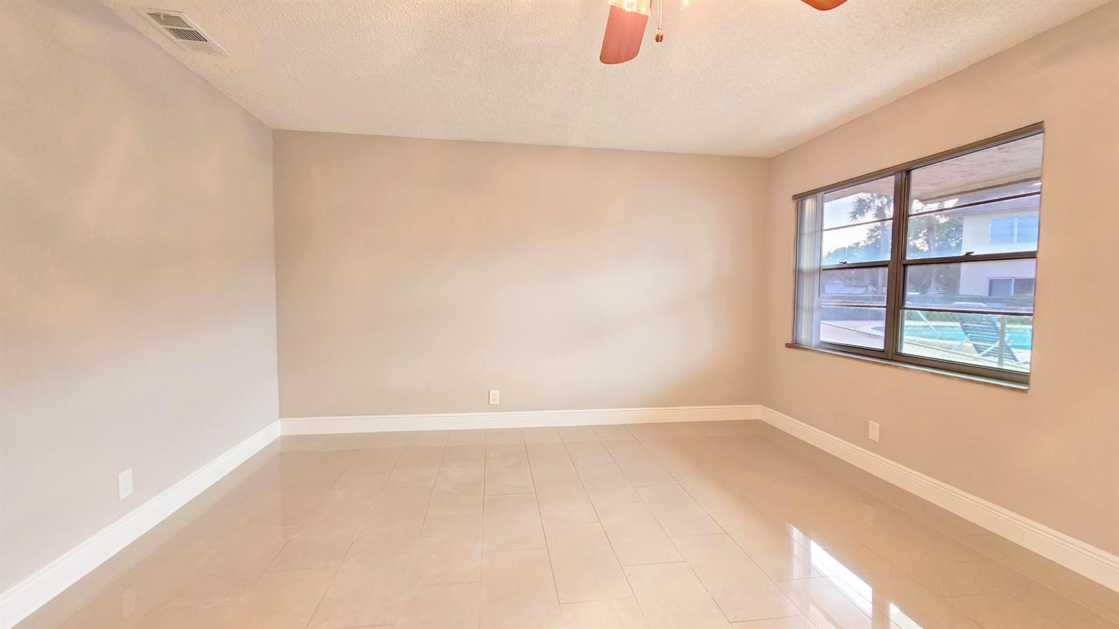 An empty room with beige walls, large light-colored floor tiles, and a window overlooking a pool — 416 Lakeside Drive # 129, Margate FL 33063, MARGATE, FL