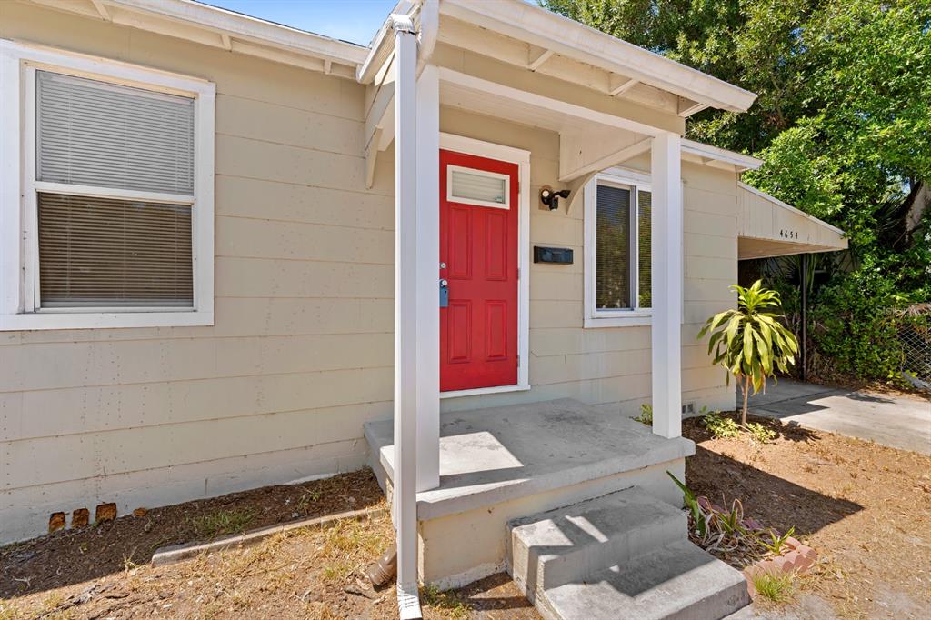 The exterior of a single-story house features beige siding, a red front door, and steps — 4654 13TH AVENUE S, ST PETERSBURG, FL