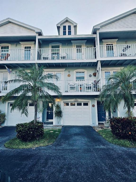 A three-story townhouse with white balconies, palm trees, and a paved driveway — 9166 BLIND PASS ROAD, ST PETE BEACH, FL