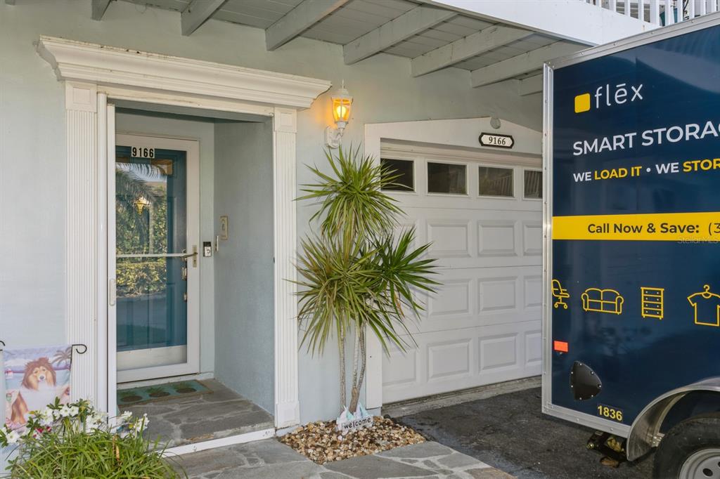 A front entryway with a blue door, a white garage door, and a storage trailer — 9166 BLIND PASS ROAD, ST PETE BEACH, FL