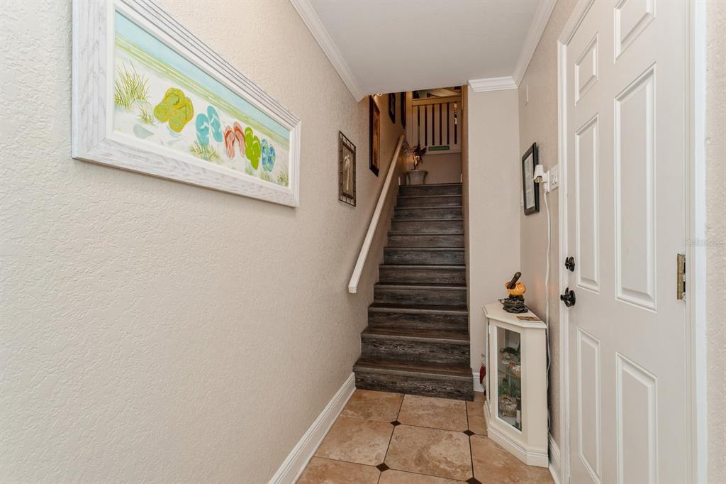 A tiled entryway features a staircase with dark wood-look steps and a framed beach painting — 9166 BLIND PASS ROAD, ST PETE BEACH, FL