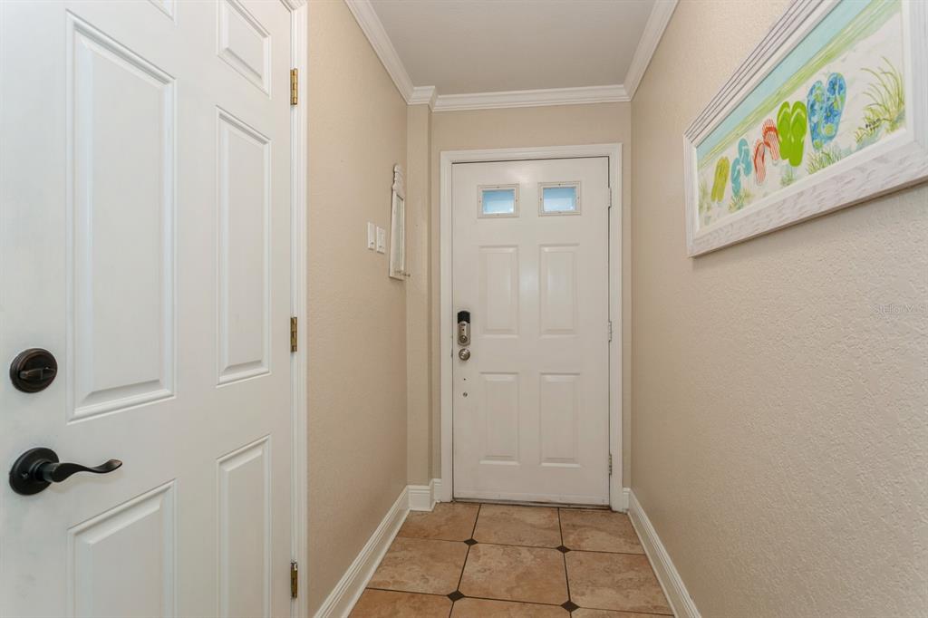 An entryway features a white front door, tile flooring, and a framed flip-flop wall art — 9166 BLIND PASS ROAD, ST PETE BEACH, FL
