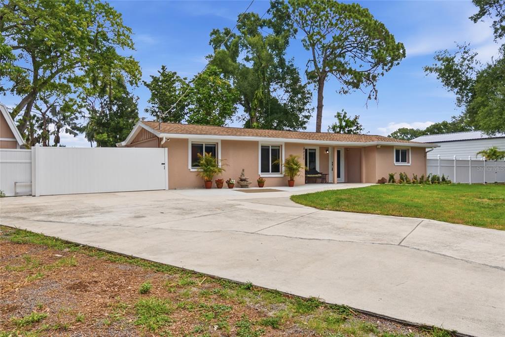 A single-story house with a tan exterior, a large concrete driveway, and white privacy fencing — 8205 WESTRIDGE DRIVE, TAMPA, FL